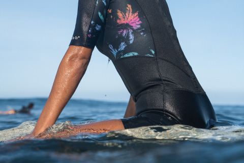 Donna seduta sulla tavola da surf, indossa la muta in neoprene.